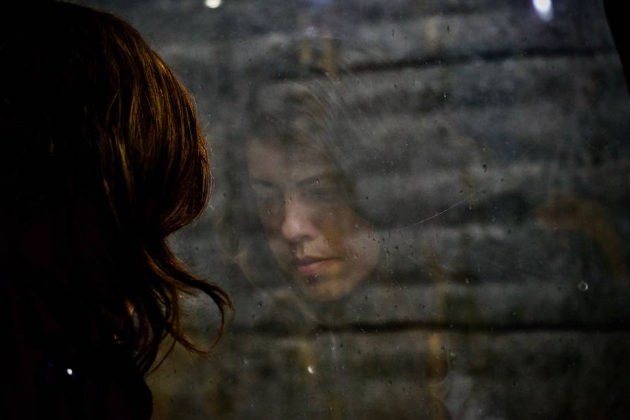 Woman with sad expression reflected in rainy window.