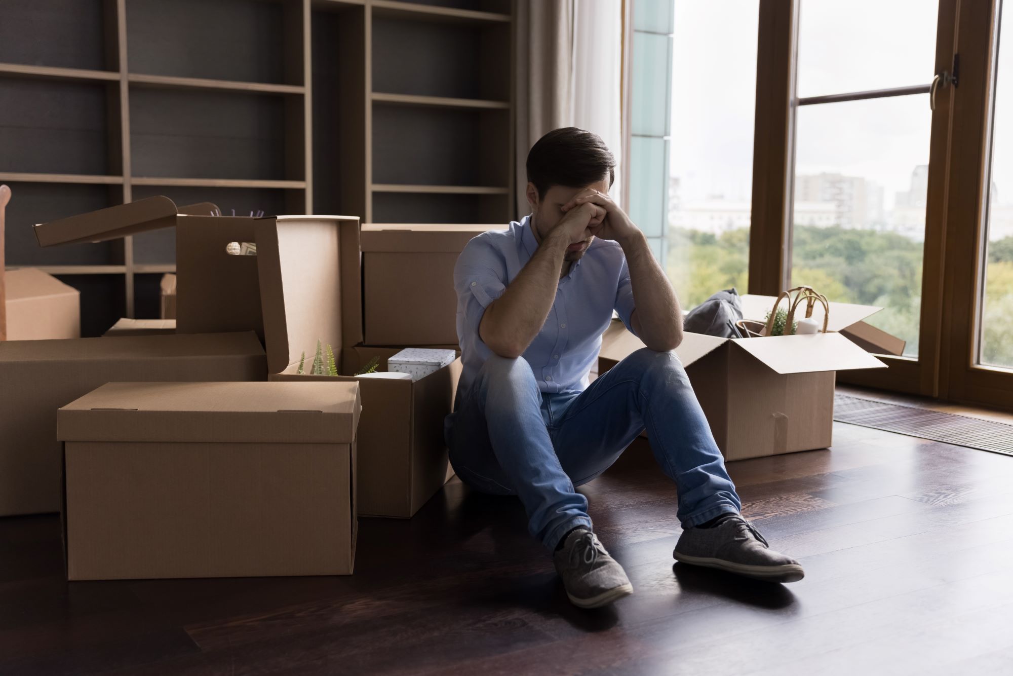 Sad man sitting on floor surrounded by boxes.